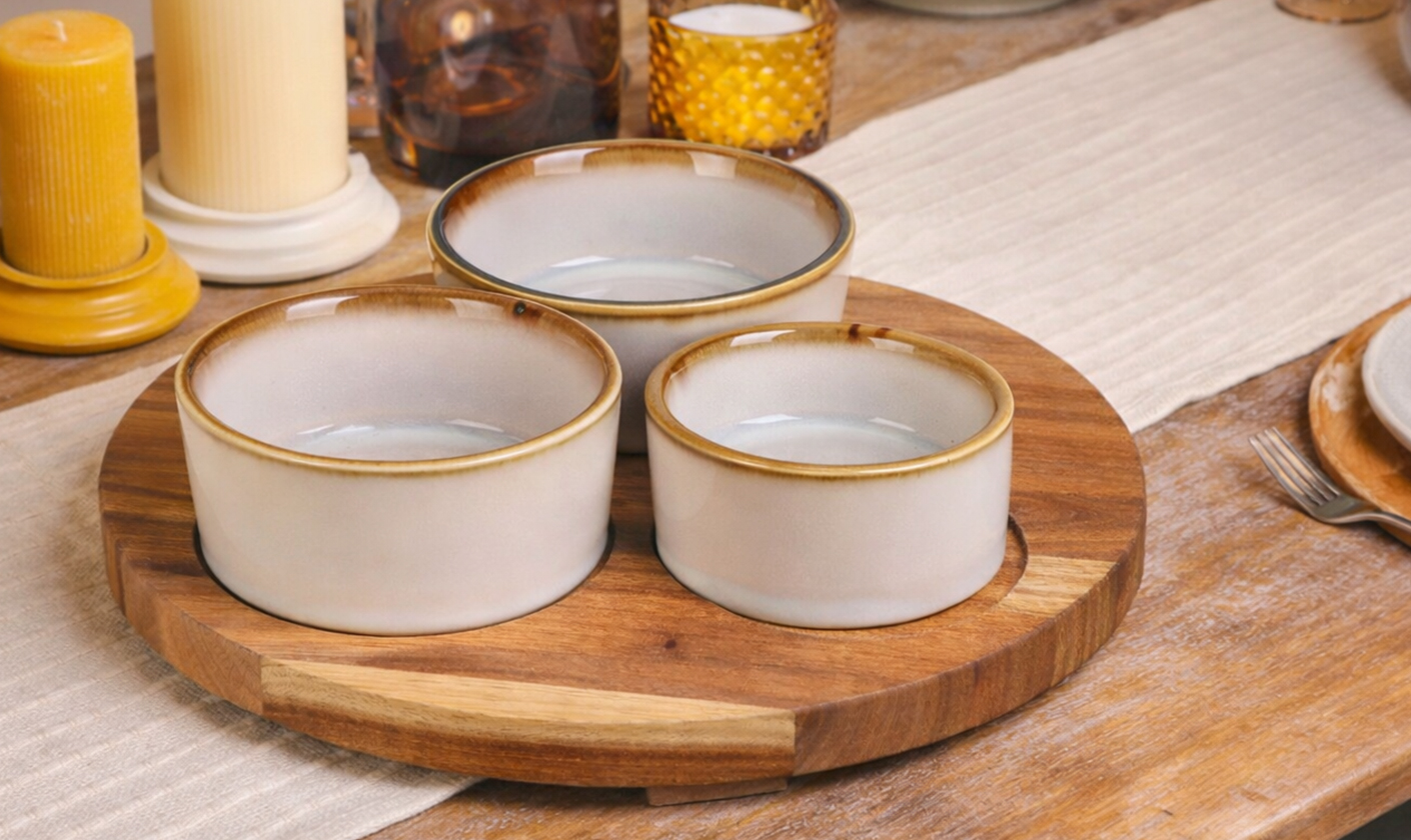 Ceramic serveware bowls displayed on a wooden board on a dining table.